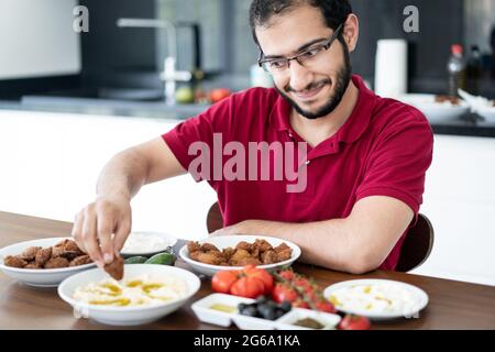 Junger Mann aus dem Nahen Osten, der allein sitzt und traditionelle Speisen isst Stockfoto
