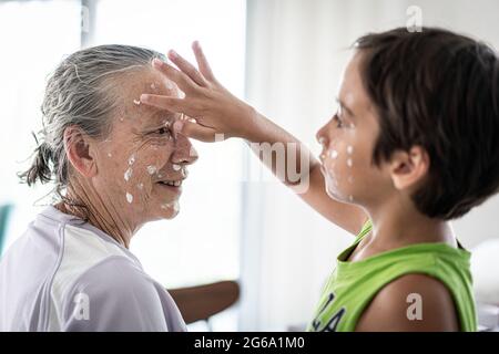 Großmutter und kleiner Junge, die Creme-Schutz auf ihr Gesicht legen Stockfoto