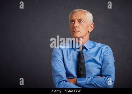 7/8 Schuß von Stattlichen älteren Mann mit Hemd und Krawatte beim Stehen mit verschränkten Armen an dunklen grauen Hintergrund. Stockfoto