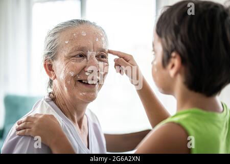 Großmutter und kleiner Junge, die Creme-Schutz auf ihr Gesicht legen Stockfoto