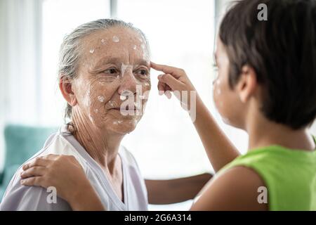 Großmutter und kleiner Junge, die Creme-Schutz auf ihr Gesicht legen Stockfoto