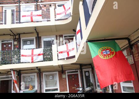 London, Großbritannien. Juli 2021. Eine portugiesische Flagge, die inmitten der mehr als 400 St George Flaggen zur Unterstützung der englischen Fußballmannschaft zu sehen ist.Kirby Estate in Bermondsey ist mit über 400 St George Flaggen zur Unterstützung der englischen Mannschaft für das verzögerte Euro 2020 Fußballturnier bedeckt. Eine Tradition der Gutsbewohner seit 2012.das englische Team besiegte die Ukraine 4-0 in Rom am 3. Juli und erreichte damit das Halbfinale gegen Dänemark, das am 6. Juli in Wembley angesetzt ist. (Foto von David Mbiyu/SOPA Images/Sipa USA) Quelle: SIPA USA/Alamy Live News Stockfoto