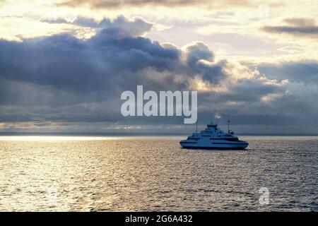 Die kleine Autofähre verkehrt zwischen dem Virtsu-Hafen Estland und der Insel Saaremaa an der Ostsee. Ruhiges Meer und Himmel mit dunklen Wolken bei Sonnenuntergang. Stockfoto