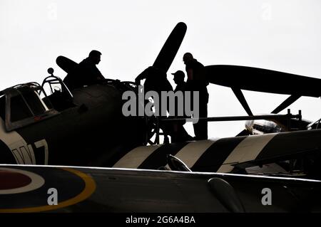 Silhouette von Ingenieuren, die an Kampfflugzeugen des Zweiten Weltkriegs im Hangar in Duxford arbeiten. Silhouetten von Mechanikern, die am Motor eines P-47 arbeiten Stockfoto
