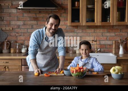 Happy niedlichen Jungen in Schürze helfen, das Abendessen vorzubereiten Stockfoto