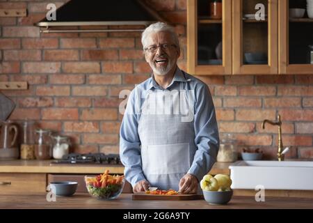 Glücklicher 70er-Jahre-Mann mit Schürze, Kochen Abendessen in der stilvollen Küche Stockfoto