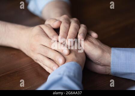 Junger Mann, der die Hände eines älteren Vaters aus der Nähe hält Stockfoto