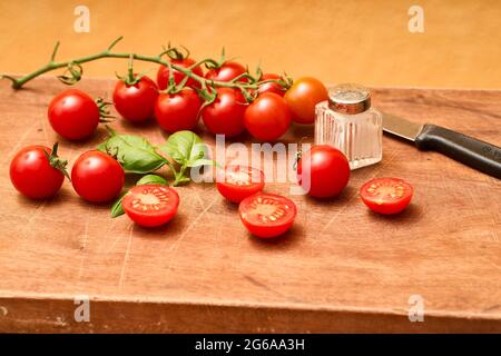 Rote Kirschtomaten, Salzstreuer-Basilikum und Messer auf EINEM braunen Holzhackbrett. Fehraltorf, Schweiz Stockfoto