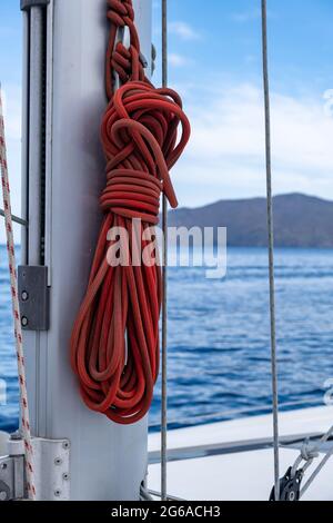 Festmachen Seile auf dem Segelboot, verwischen Seestücke Hintergrund. Rotes Segelseil auf dem Schiffsmast. Nahaufnahme, vertikal. Segelboot-Kreuzfahrt in Aege Stockfoto