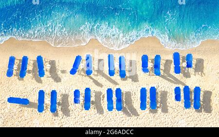 Zwei Reihen leerer blauer Sonnenliegen am gelben Sandstrand, Luftpanorama von direkt oben Stockfoto