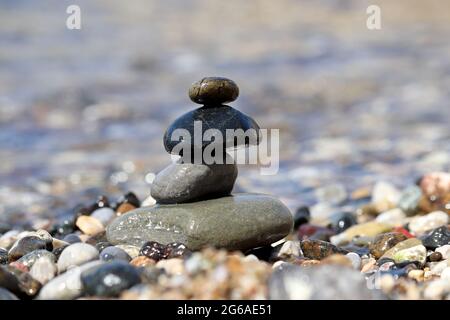 Turm aus Kieselsteinen vor dem Hintergrund der Meereswellen. Sommerurlaub, Balance und Relax-Konzept Stockfoto