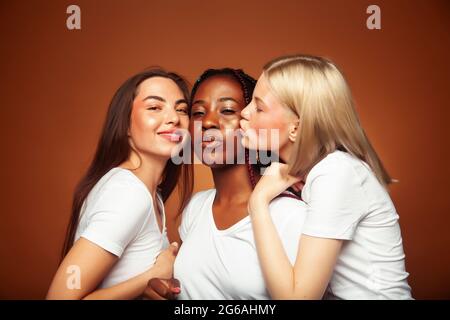 Junge hübsche kaukasische, afro, skandinavische Frau posiert fröhlich zusammen auf braunem Hintergrund, Lifestyle diverse Nationalität Menschen Konzept Stockfoto
