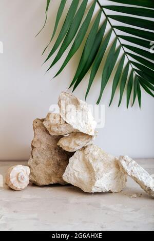 Leerer Turm mit Podeststeinen. Graue Steine Podest-Display auf beigem Hintergrund aus Muschelsteinen Palmblatt. Abstraktes Hintergrundmockup für Stockfoto