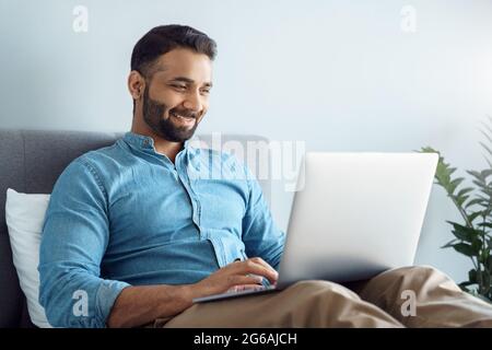 Glücklich lächelnder indischer Geschäftsmann, der von zu Hause aus mit einem Laptop arbeitet Stockfoto