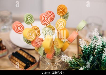 Süße bunte Fruchtbonbons mit Zucker und natürlichem Saft auf Holzstäben im Glasglas an der Süßigkeitenbar. Stockfoto