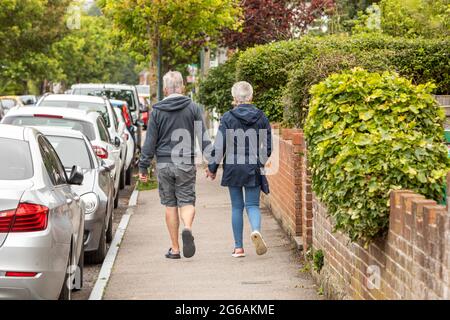 Ein Paar mittleren Alters, das Hand in Hand auf einem städtischen Fußweg läuft Stockfoto