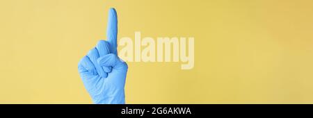 Der Arzt hält den Daumen in einem schützenden medizinischen Handschuh hoch Stockfoto
