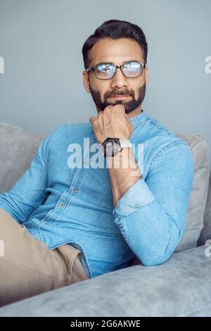 Nachdenklicher indischer Geschäftsmann, der auf dem Sofa sitzt und zur Seite schaut Stockfoto