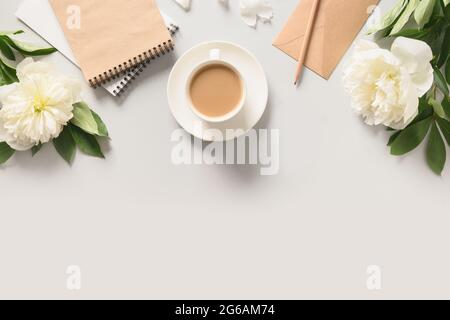 Sommerfrühstück mit Kaffeetasse, Skizzenbuch für die Planung und weißen Pfingstrosen-Blumen auf grauem Schreibtisch. Blick von oben, flach liegend. Stockfoto
