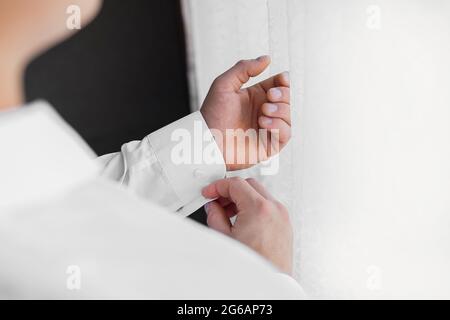 Ein Mann in einem weißen Hemd umklammelt seine Ärmel beim Licht vom Fenster stehend. Stockfoto