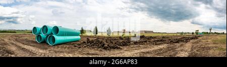 Gestapeltes Wasserhauptrohr mit Glockenanschluss neben einem freiliegenden Graben zur Installation Stockfoto