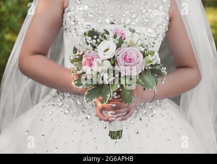 Die Hände der Braut in einem weißen Hochzeitskleid halten einen Blumenstrauß aus der Nähe. Stockfoto