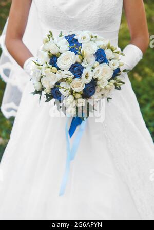 Braut im weißen Hochzeitskleid hält einen Blumenstrauß mit weißen und blauen Rosen aus nächster Nähe. Stockfoto