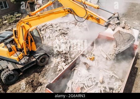 Bagger beladen Bauabfälle in LKW zur Entfernung von der Baustelle. Abriss von baufälligen Wohnungen für Neuentwicklung, Luftaufnahme Stockfoto