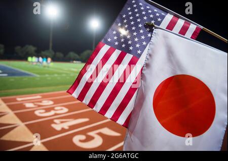 Flutlicht-Ansicht der US- und japanischen Flaggen, die vor den nummerierten Spuren an der Startlinie einer roten Laufstrecke zusammenfliegen Stockfoto