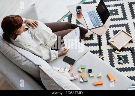 Draufsicht auf eine schwanger afroamerikanische Frau, die den Haushaltsbericht liest, während sie von zu Hause aus arbeitet und von Spielzeug umgeben ist, Platz zum Kopieren Stockfoto