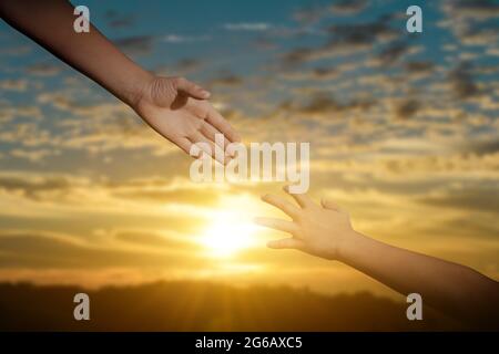 Ein Konzept zur Hilfestellung geben. Die Hand reicht, um sich über den Hintergrund des Sonnenuntergangs gegenseitig zu unterstützen, zu hoffen und zu unterstützen. Stockfoto