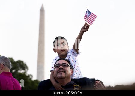 Gilbert Rodriguez, sechs Jahre alt, aus Long Beach, Kalifornien, hält die US-Nationalflagge auf den Schultern seines Vaters Eddie Rodriguez, während US-Präsident Joe Biden während einer Feier des Unabhängigkeitstages in Washington, DC, USA, am 04. Juli 2021 auf dem South Lawn des Weißen Hauses eine Rede hält. Stockfoto