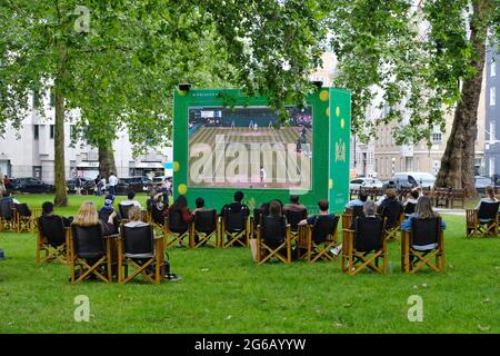 Die Menschen genießen öffentliche Vorführungen des Wimbledon-Tennisturniers auf dem Berkerley Square in Mayfair, als einer von vielen Outdoor-Bildschirmen in der Hauptstadt Stockfoto