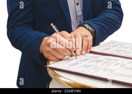 Die Hände des Mannes des Bräutigams setzten die Unterschrift in der Zeitschrift über die Zustimmung zur Hochzeit auf. Stockfoto