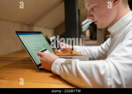 Geschäftsmann mit Telefon, Laptop und Karte, der elektronische Zahlungen an seinem Arbeitsplatz abwickte Stockfoto