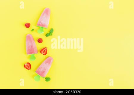 Flaches Lay mit fruchtigem rosa gefrorenem Sorbet Eis auf grüner Plastikstick Sammlung mit Schnitten von Erdbeere, Minzblätter auf gelbem Hintergrund. Gefroren Stockfoto