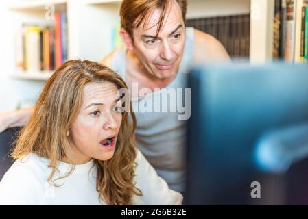 Ein Paar mittleren Alters, das zu Hause überrascht auf den Computer schaut Stockfoto