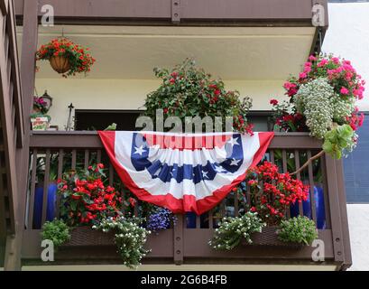 Am Independence Day in Monterey, CA, hängt ein leuchtend rot-weiß-blaues Gestrümmer mit Sternen und Streifen vom Geländer eines kleinen Balkons. Stockfoto