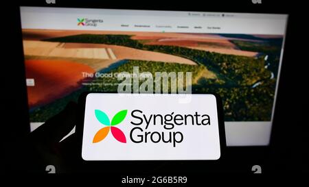 Person, die Mobiltelefon mit Logo des Schweizer Landwirtschaftsunternehmens Syngenta Group auf dem Bildschirm vor der Business-Webseite hält. Konzentrieren Sie sich auf die Telefonanzeige. Stockfoto