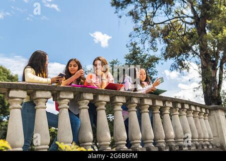 Teenager-Mädchen interagieren mit ihren Handys auf einer Terrasse unter blauem Himmel. Bildungs- und Technologiekonzept Stockfoto