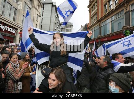 Ein Protestler auf den Schultern eines Freundes singt und schwenkt während des Protestes eine israelische Flagge.Pro-israelische Demonstranten versammeln sich vor der israelischen Botschaft in der High Street Kensington, um den am 21. Mai vereinbarten Waffenstillstand zu unterstützen. Eine kleine Gruppe von Palästinensern kam zur Gegendemonstration der israelischen Demonstration, doch die Polizei bildete eine Absperrung zwischen den beiden Massen, um jegliche Gewalt zu vermeiden. Stockfoto