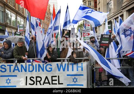 Während der Demonstration winken Demonstranten mit Fahnen und halten ein Transparent mit der Aufschrift "Standing with Israel".Pro-israelische Demonstranten demonstrieren vor der israelischen Botschaft in der High Street Kensington, um den am 21. Mai vereinbarten Waffenstillstand zu unterstützen. Eine kleine Gruppe von Palästinensern kam zur Gegendemonstration der israelischen Demonstration, doch die Polizei bildete eine Absperrung zwischen den beiden Massen, um jegliche Gewalt zu vermeiden. Stockfoto