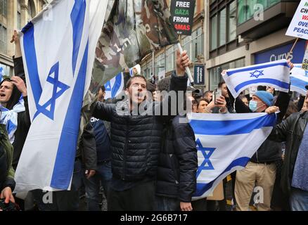 Pro-israelische Anhänger schwingen während des Protestes Fahnen, halten Plakate fest.Pro-israelische Demonstranten demonstrieren vor der israelischen Botschaft in der High Street Kensington, um den am 21. Mai vereinbarten Waffenstillstand zu unterstützen. Eine kleine Gruppe von Palästinensern kam zur Gegendemonstration der israelischen Demonstration, doch die Polizei bildete eine Absperrung zwischen den beiden Massen, um jegliche Gewalt zu vermeiden. Stockfoto