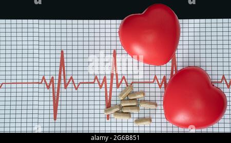 Layout eines Elektrokardiogramms, einige Pillen und zwei herzförmige Modelle auf schwarzem Hintergrund Stockfoto