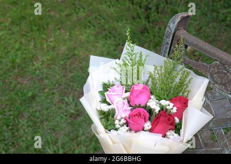 Auf einem rustikalen Stahlstuhl ruhen Bouquet aus frischen roten und rosafarbenen Rosen. Speicherplatz kopieren. Stockfoto
