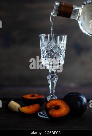 Pflaumendka wird in ein Glas mit frischen Pflaumen auf einem Tisch gegossen Stockfoto