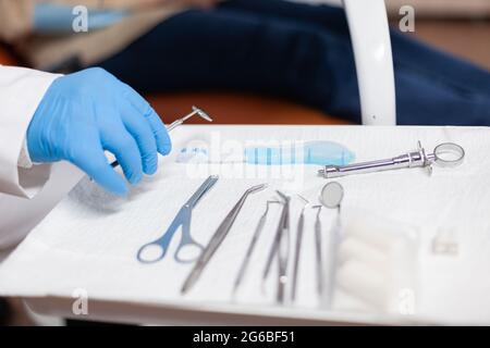 Nahaufnahme Stomatolog Einnahme von USSTENSEN für zahnärztliche Intervention der älteren Frau. Ältere Patienten während der medizinischen Untersuchung mit Zahnarzt in Stomatologie Büro mit orangen Geräten. Stockfoto