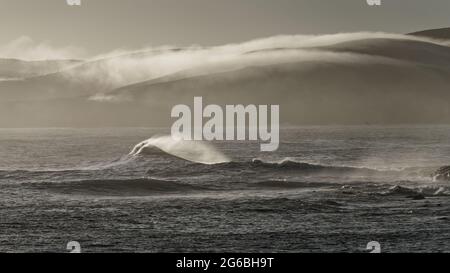 Beleuchtete Wolken und Wellen brechen bei Sonnenaufgang in Curio Bay, den Catlins, Südinsel, Neuseeland. Stockfoto