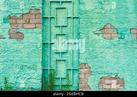 Malen Sie grüne Wand Grill rustikalen alten Hintergrund.Gebäude grüne Wand mit einer Tür Metall Grill.eine bröckelnde Wand blickt auf die Steine an einem Sommertag.Nahaufnahme Stockfoto