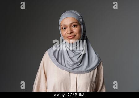 Frau aus dem Nahen Osten in Hijab lächelt und blickt isoliert auf grauen Hintergrund auf die Kamera Stockfoto